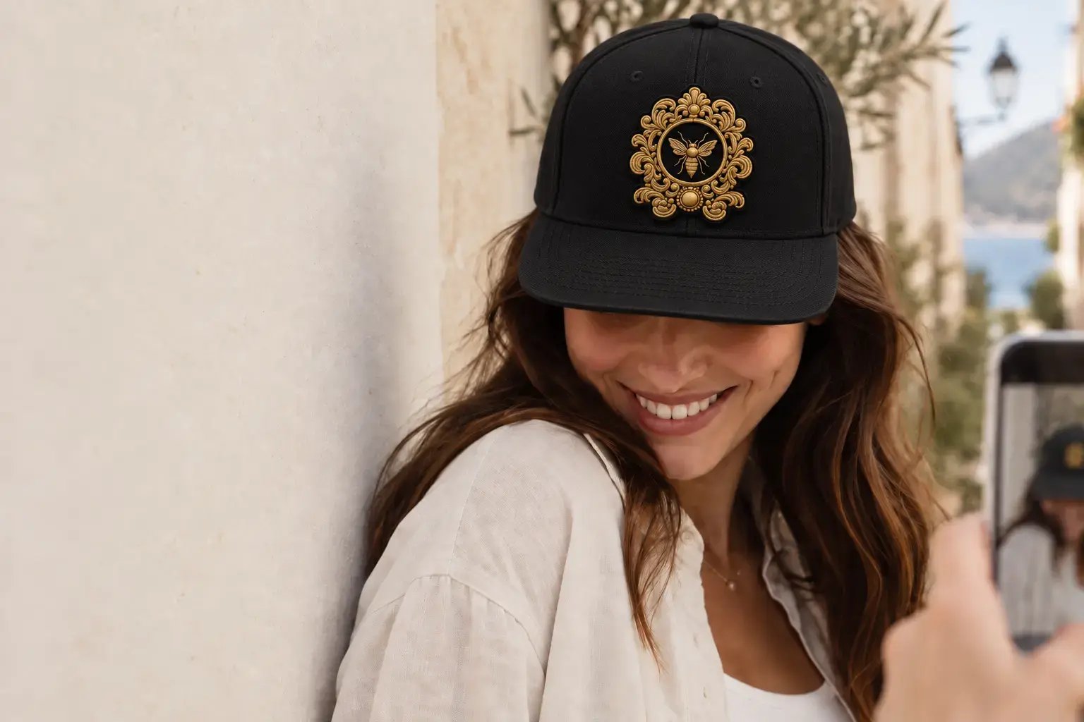 Woman wearing a black Signature Lab snapback with an ornate gold bee crest, photographed outdoors. Woman wearing a black Signature Lab snapback with an ornate gold bee crest, photographed outdoors.
